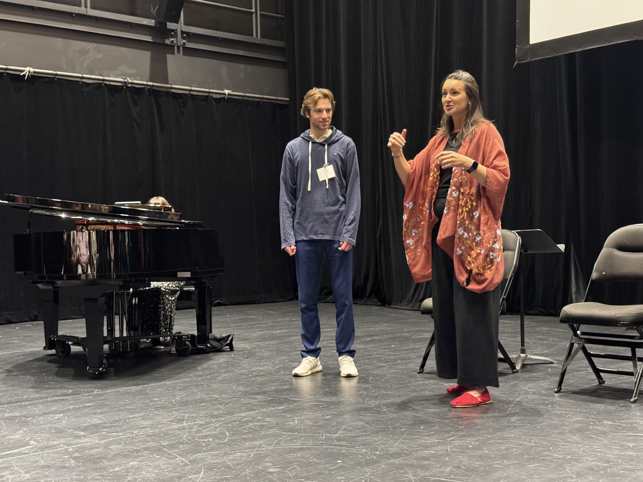 A singer and coach working in a rehearsal studio beside a grand piano.