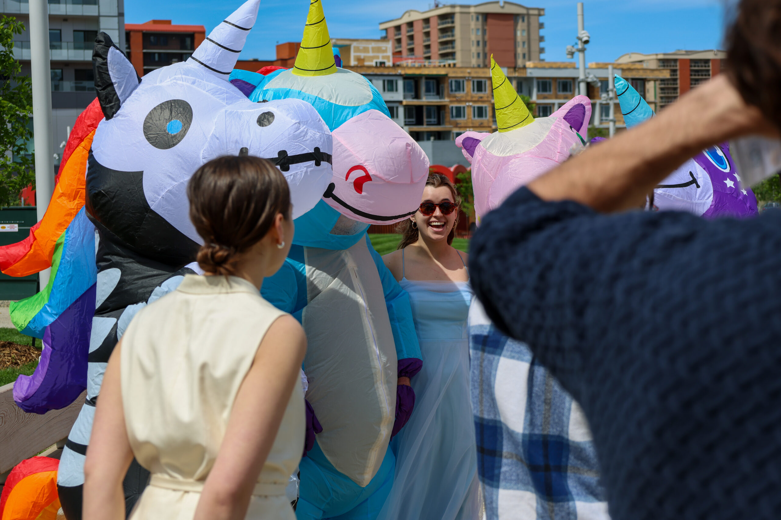 Artists laughing outdoors alongside colourful inflatable unicorn costumes.